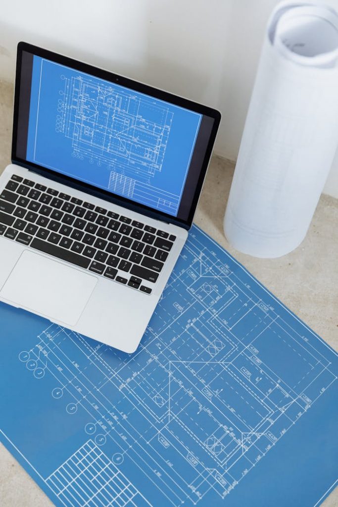 pexels photo 8470810 Laptop showing engineering blueprint with rolled paper and drawings on table.
